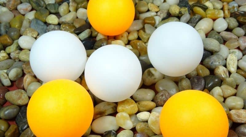 Weiße und orange Tischtennisbälle auf Steinen liegend