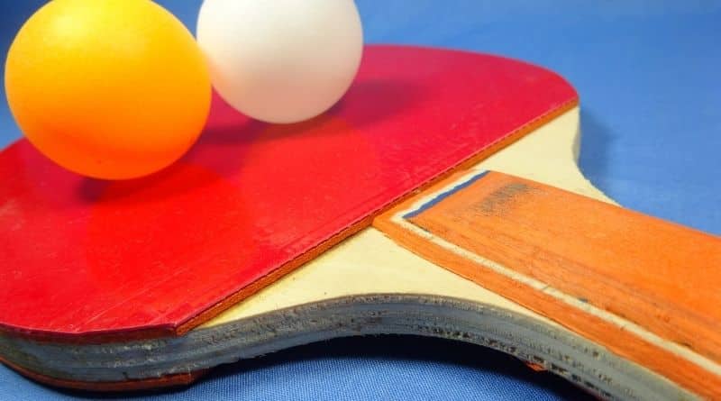 Ein Tischtennisschläger liegt auf einer blauen Platte und auf dem Schläger 2 Bälle